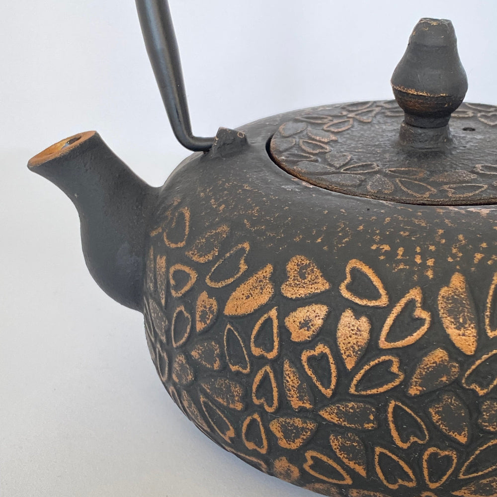 Black teapot with gold heart patterns on a white background