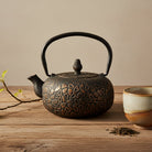 Decorative teapot and ceramic cup on a wooden surface with a branch and leaves.