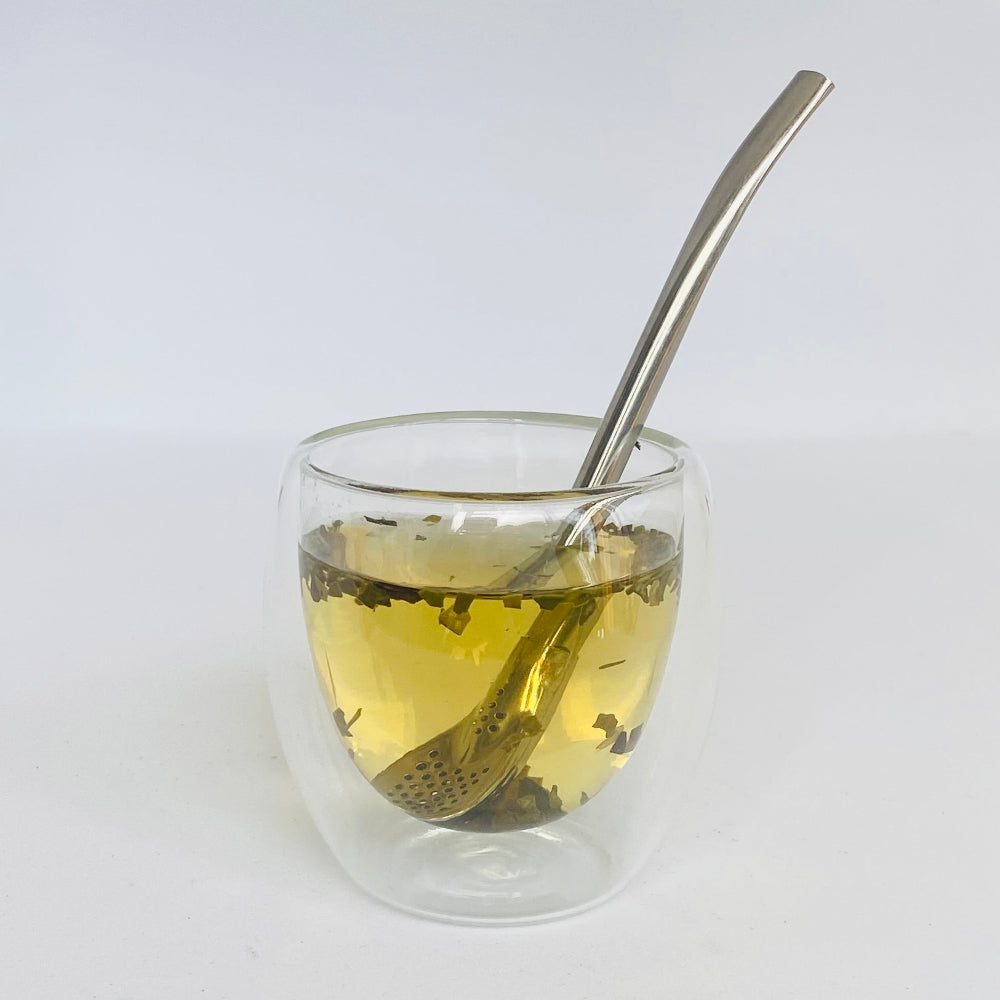 Clear glass with iced tea and a metal Bombilla spoon on a white background