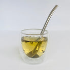 Clear glass with iced tea and a metal Bombilla spoon on a white background