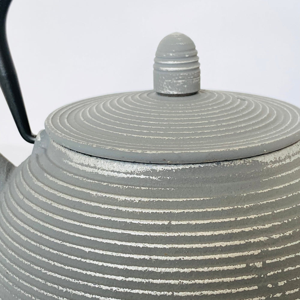Gray ceramic teapot with ribbed design and black handle on a white background