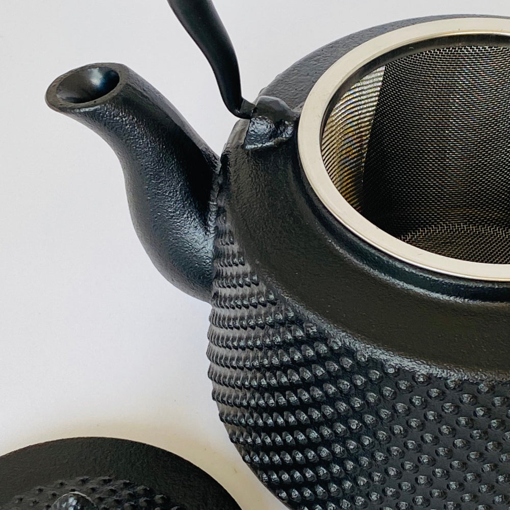 Black textured teapot with a mesh filter on a white background